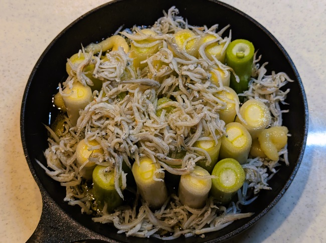 スキレットに縦に並べた長ネギの上にしらすをのせる
