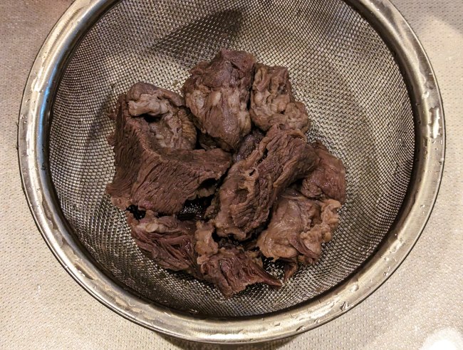 下茹でした牛すじを水洗いしアクを洗い流す