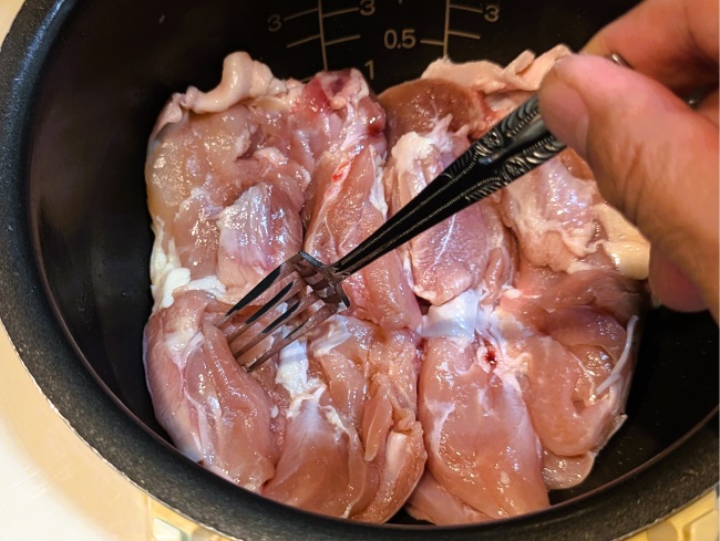 炊飯器に入った鶏肉をフォークで刺す